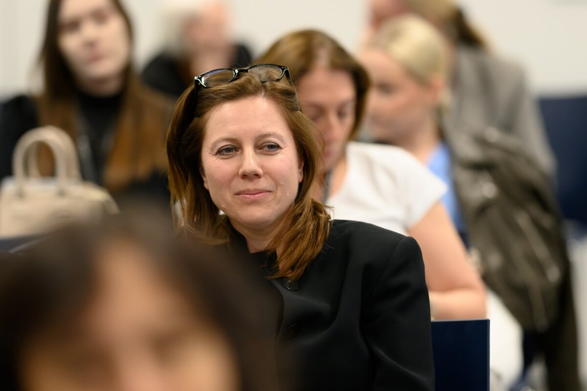Focus on a woman in the audience of a conference at SWPS University with other women in the background
