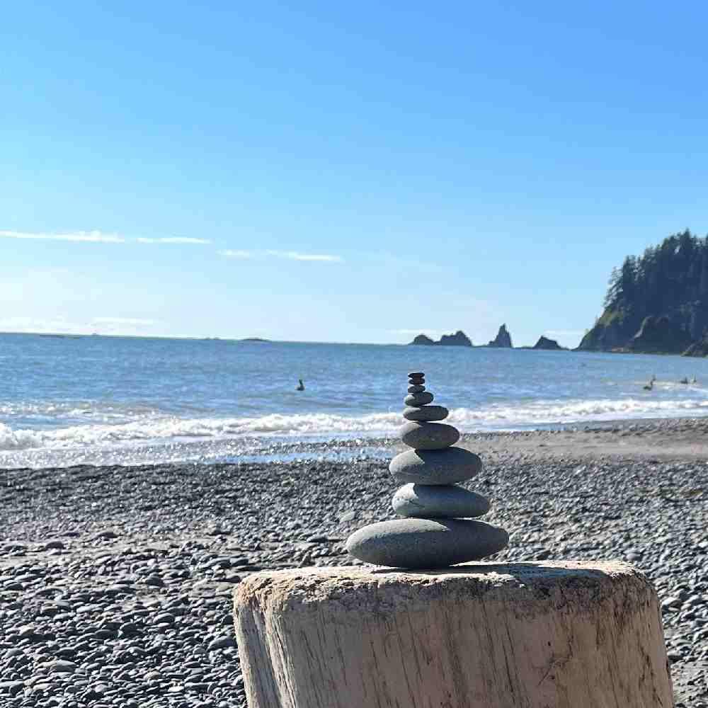 Inukshuk made of round stones, placed on a tree trunk, on a beach