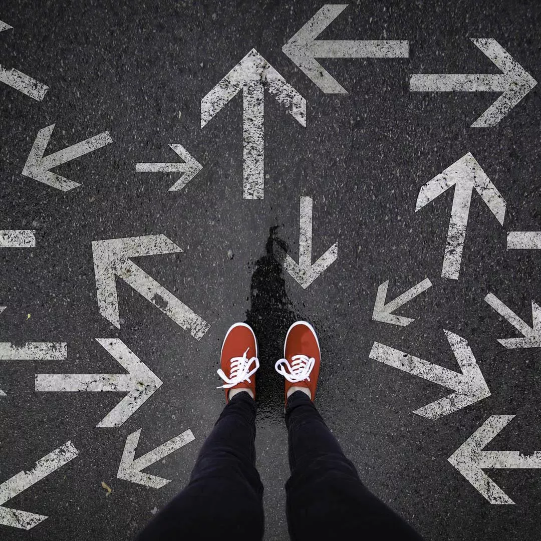 human legs on asphalt among arrows pointing out in different directions