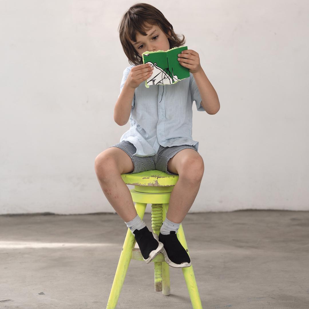 a boy sitting on a stool reading a book
