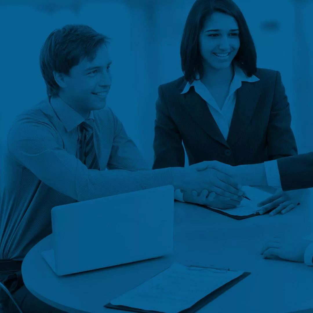 Young professional man and woman sitting at a table shaking customer's hand