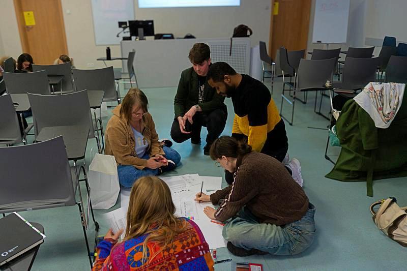 Five students sit on the floor drawing on a large piece of paper
