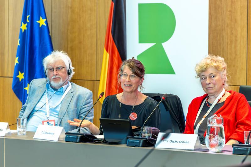 One male and two female professors sit behind a table at a conference