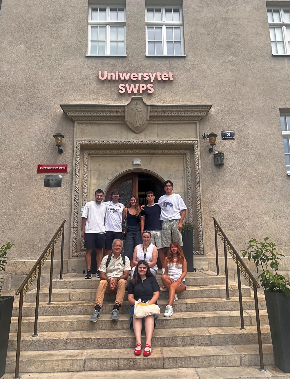 Group of students and academics sit on the steps leading to the building of USWPS in Kraków