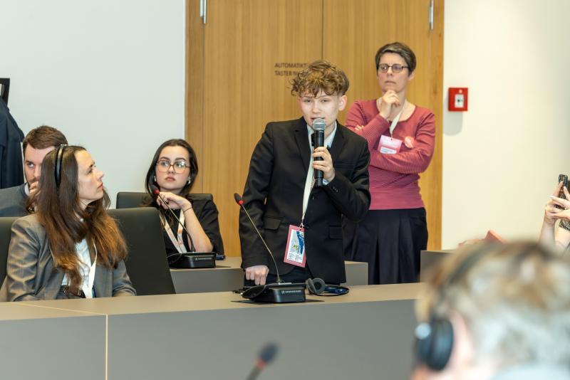 Male student with curly hair asks a question during a conference