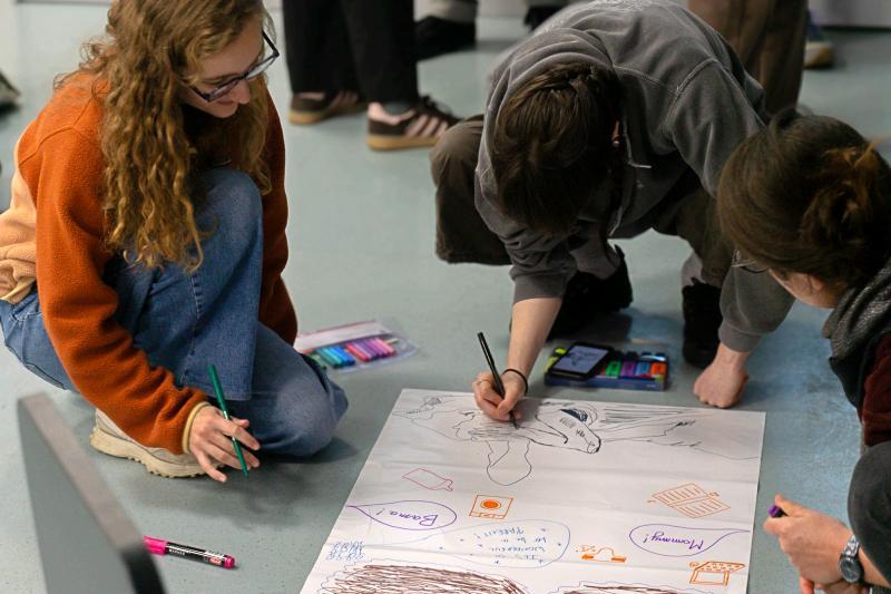 Three students sit on the floor and draw on a flipchart page