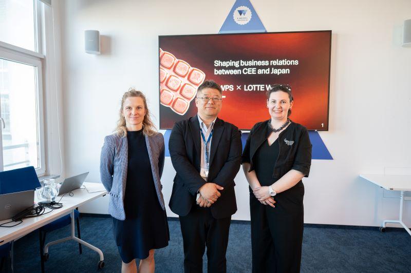 Two women and a man are standing in a room, behind them there is a monitor with a presentation