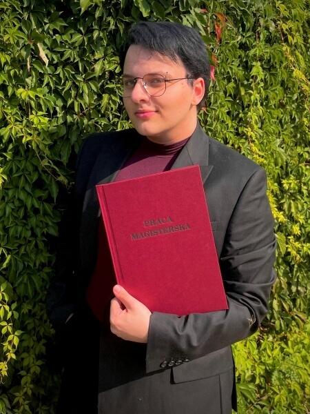 Ignacy Maliszewski, SWPS University graduate, proudly holding his completed master's thesis.