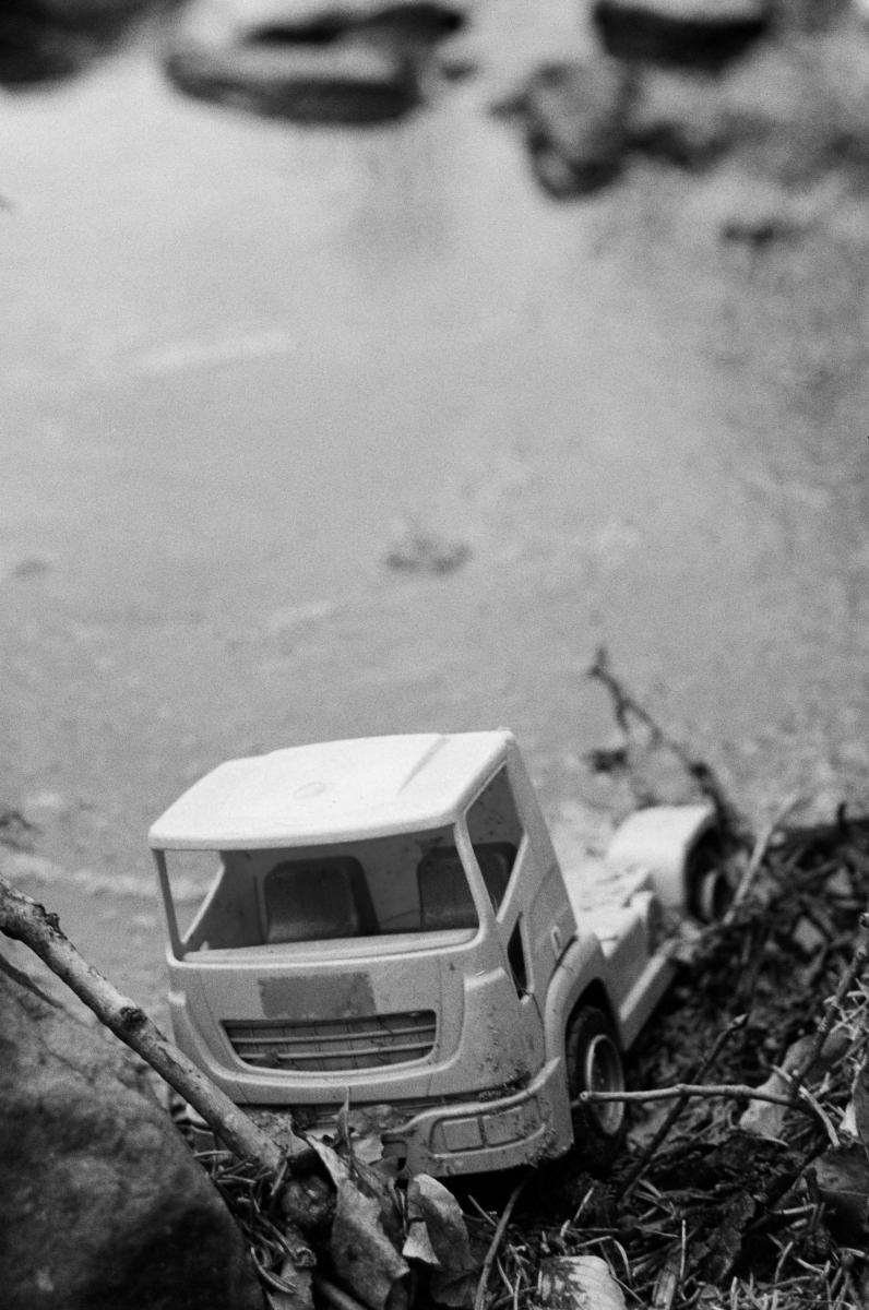 A black-and-white photo of a plastic toy truck at the water's edge.