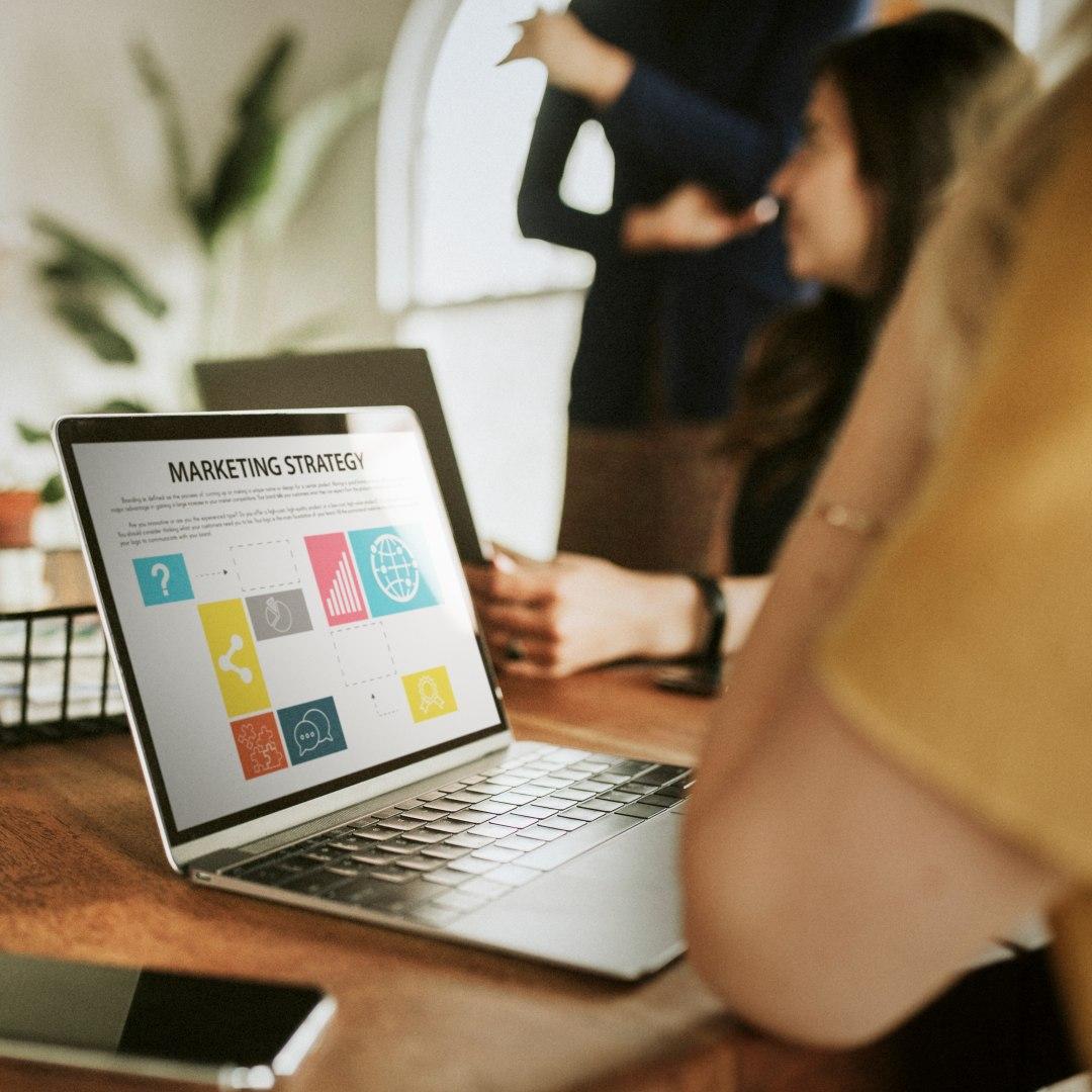 Open laptop on table showing marketing presentation, people in the background
