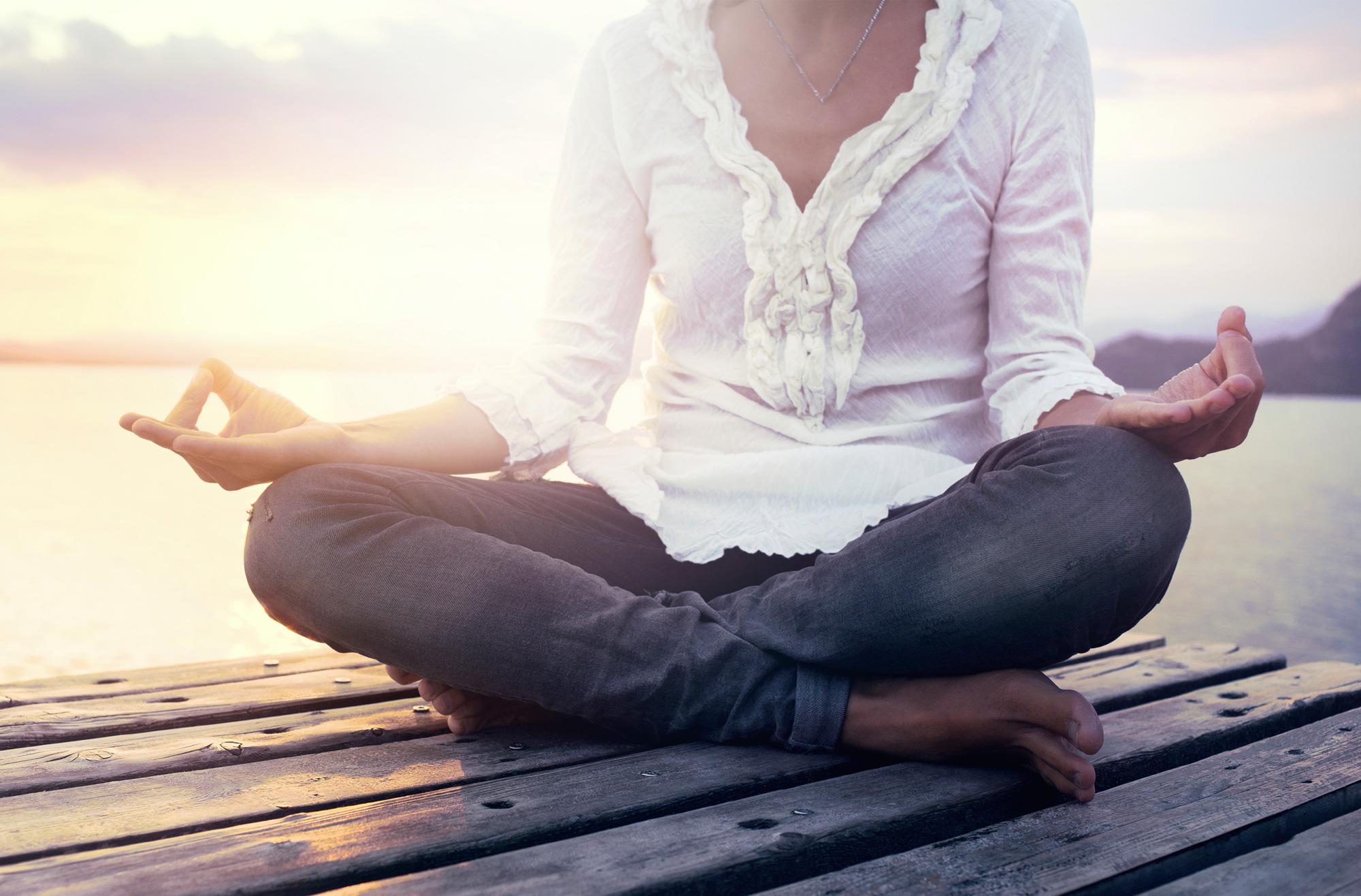 woman sitting cross-legged in meditating position on deck on lake
