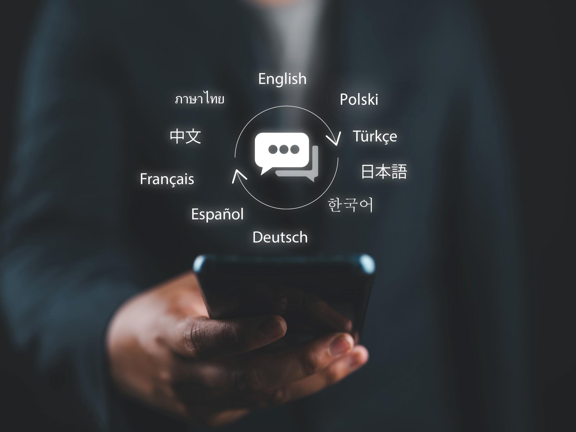 A hand holds a smartphone. Above the device, a communicator symbol radiates, surrounded by the names of various world languages, representing the diversity of global communication.