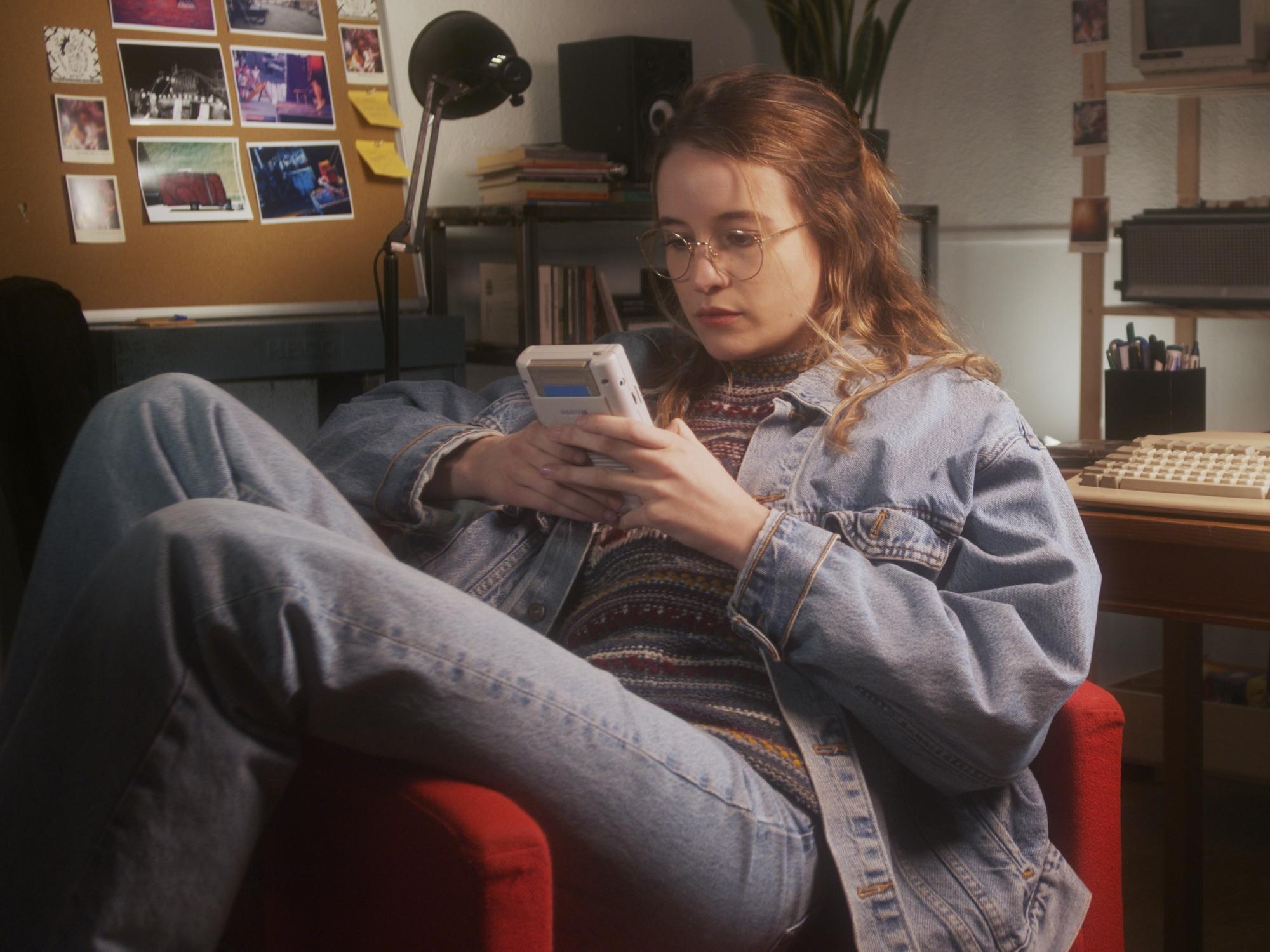 Teenage girl playing a Game Boy in a 1990s-style bedroom