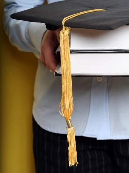 Student holds books covered with graduation cap