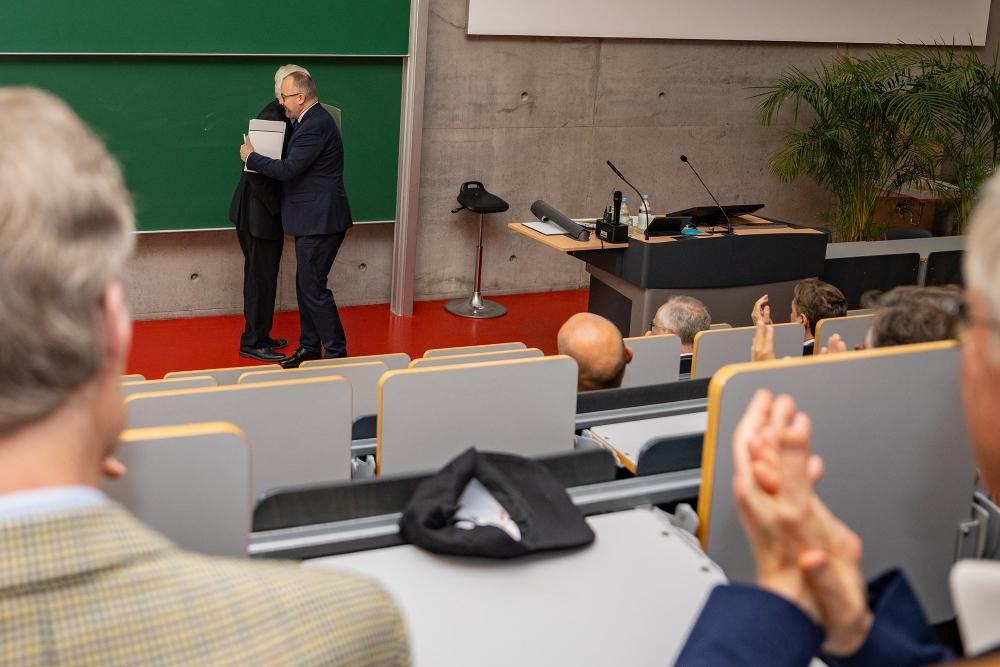 Ceremony audience in the foreground, with Adam Bodnar and Andreas Zimmermann embracing in the background after the diploma presentation.