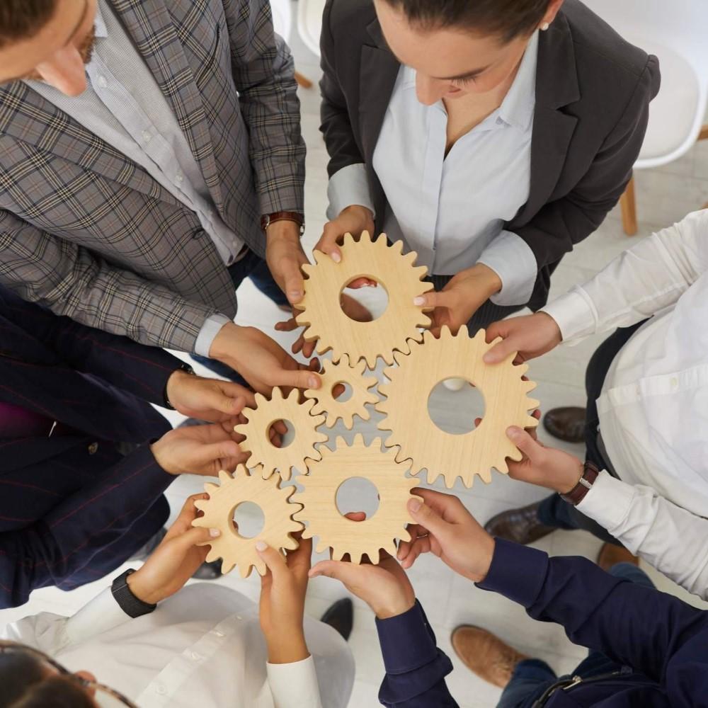 People holding wooden gears, symbolizing partnership and collaboration, like parts of a smoothly running machine.