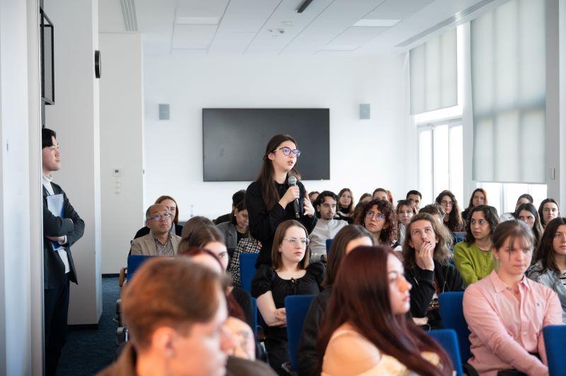 A room full of students, one of the students stands and speaks into a microphone
