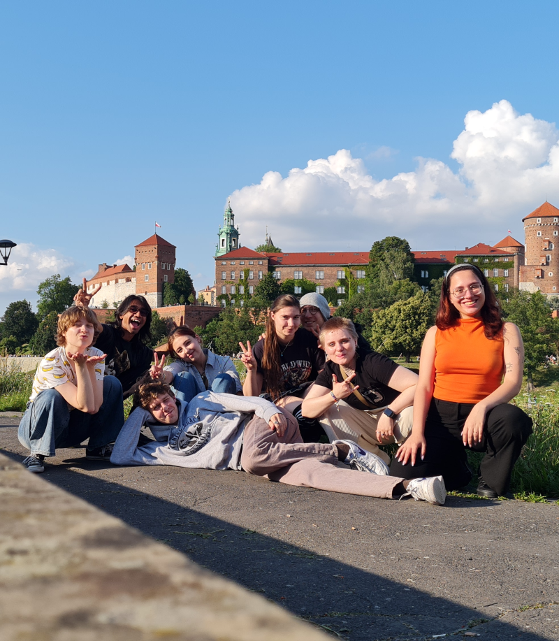 Eight smiling, relaxed students pose for a photo against the backdrop of Wawel Castle
